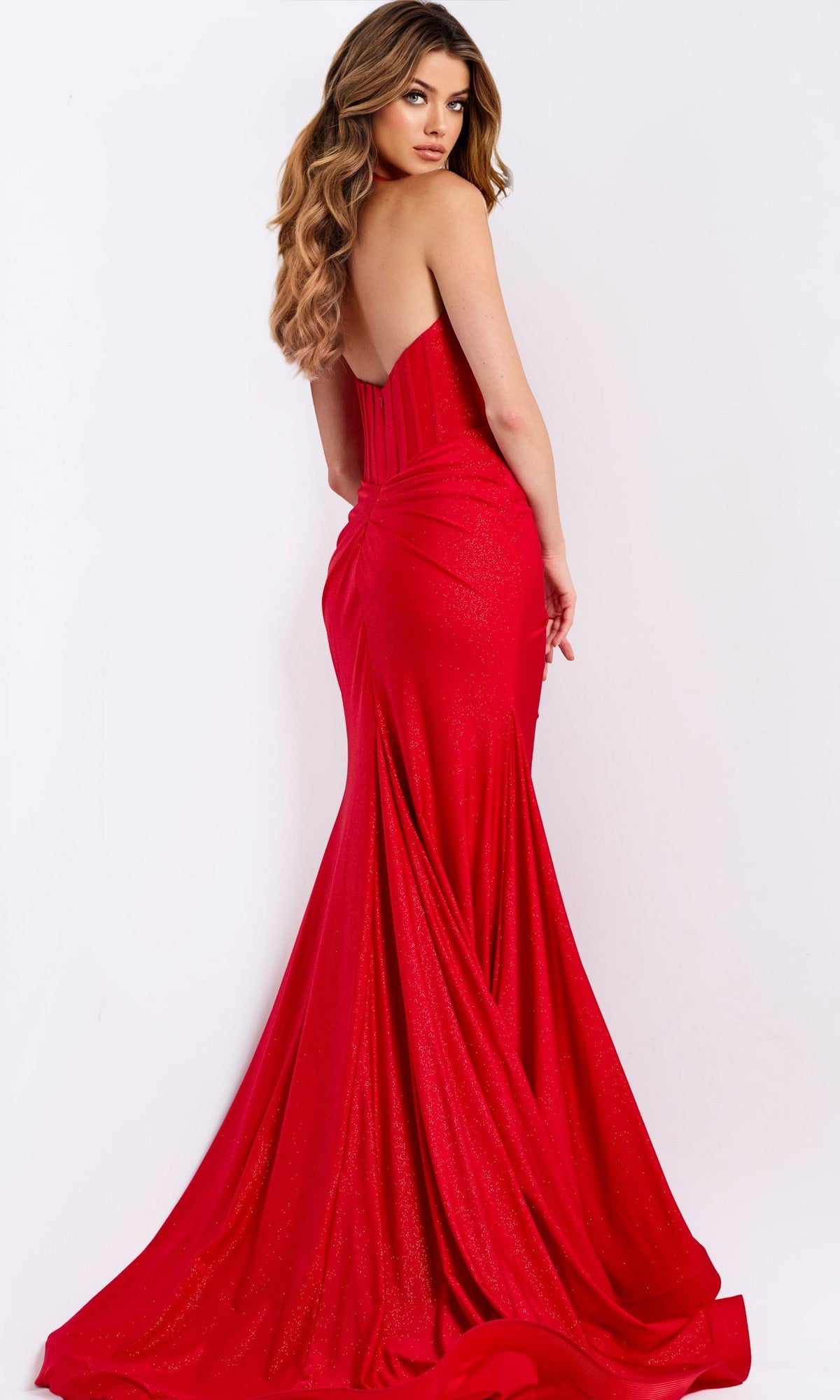 Woman wearing the Jovani 46489 Long Prom Dress—a strapless, floor-length red gown with a plunging v-neckline and long train—stands against a plain white background, looking over her shoulder.
